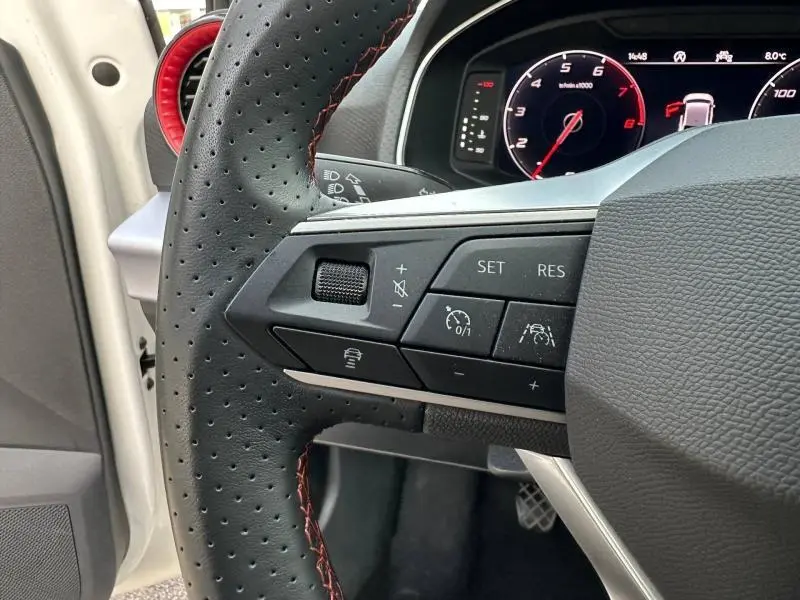 Gros plan sur le volant perforé avec commandes intégrées du SEAT Ibiza 1.0 TSI FR blanc Nevada, tableau de bord numérique en arrière-plan.