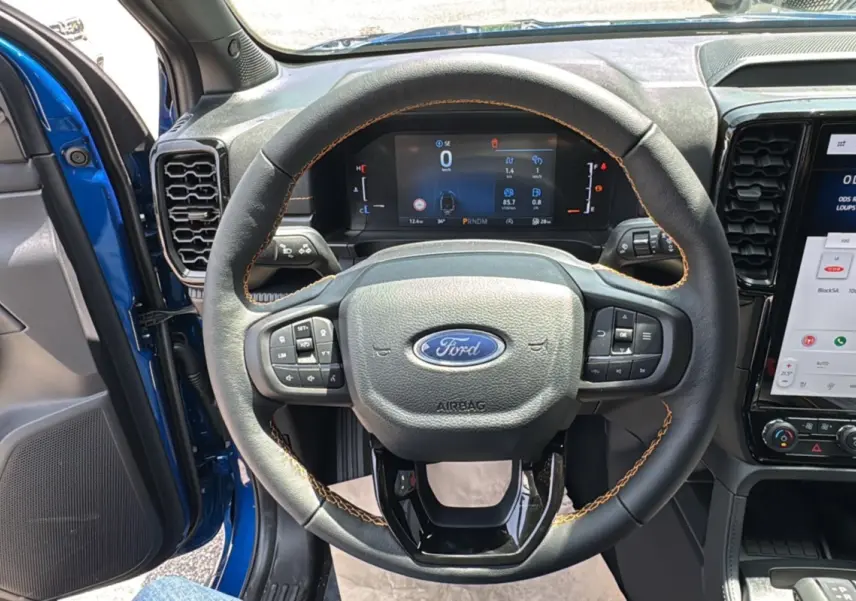 Vue intérieure centrée sur le volant cuir noir avec surpiqûres marron du Ford Ranger bleu lightning 2025 Wildtrak X Pack X Rideau.
