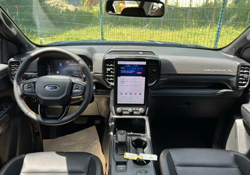 Vue intérieure avant du Ford Ranger Wildtrak X 2025, tableau de bord noir avec écran tactile vertical et volant multifonctions cuir.