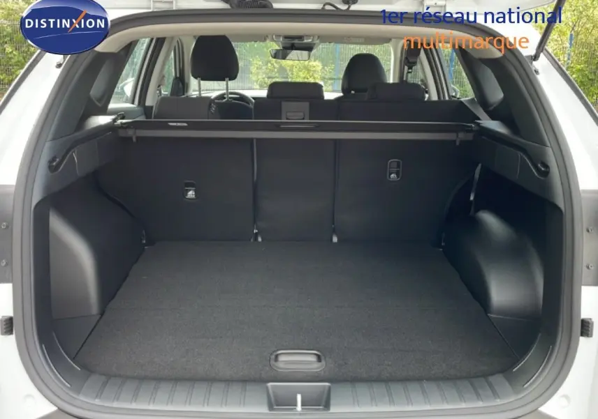 Coffre ouvert d’un Hyundai Tucson blanc atlas, vue arrière montrant l’espace de chargement et les sièges arrière rabattus.