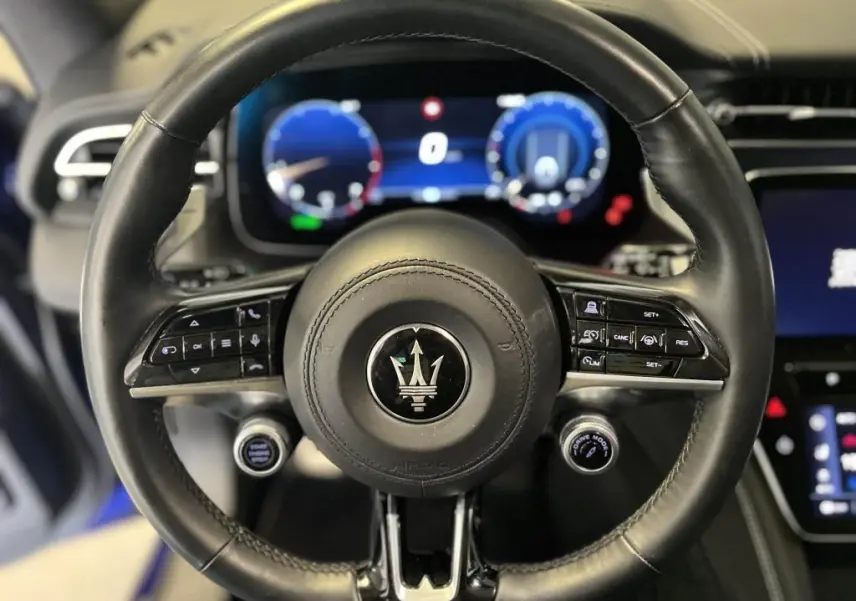 Gros plan sur le volant cuir multifonction de la Maserati Grecale bleu, avec commandes de régulateur et bouton Drive Mode visible.