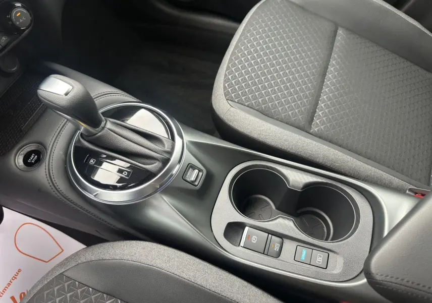 Gros plan sur la console centrale du Nissan Juke gris, avec levier de vitesse automatique et sièges en tissu noir.