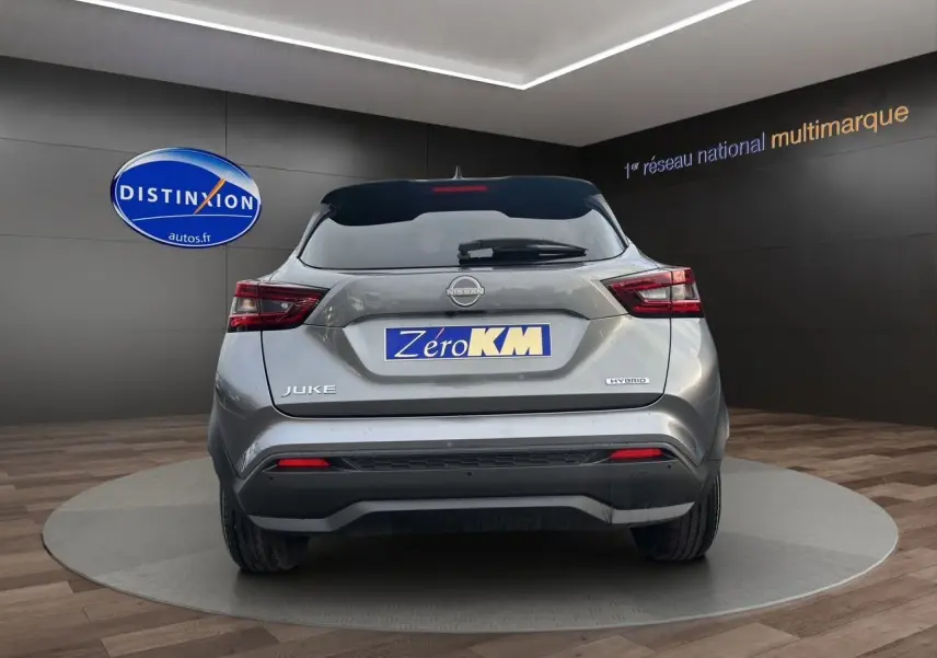Vue arrière d'un Nissan Juke gris squale hybride, avec feux LED et logo Zero KM visible sur fond showroom.