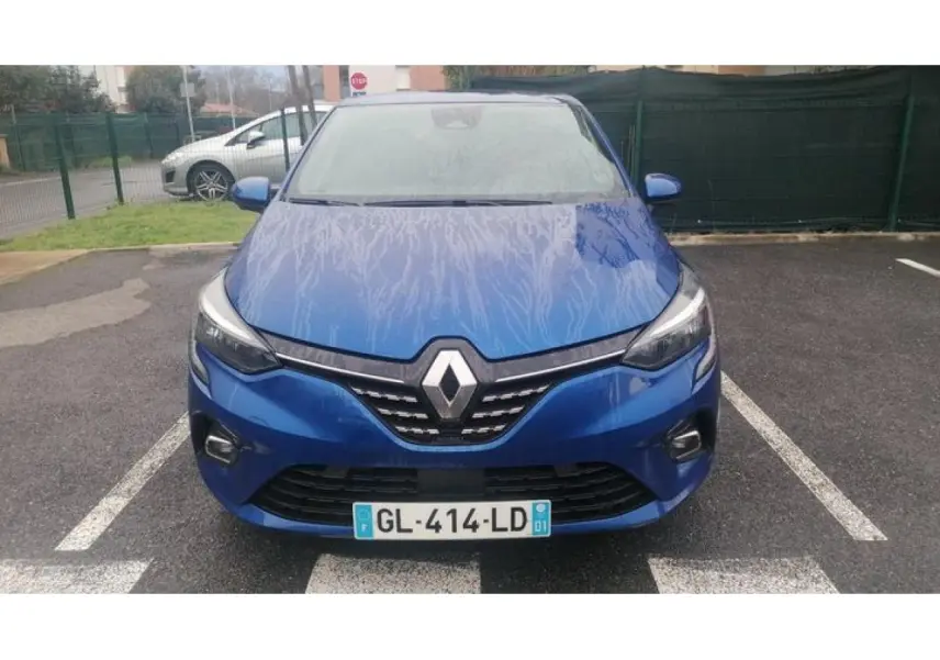 Vue avant d'une Renault Clio 2021 bleu Iron avec calandre chromée et phares LED allumés sur parking.