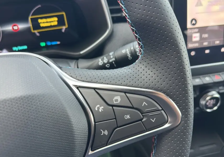 Gros plan sur le volant cuir perforé de la Renault Clio V E-Tech 145 Esprit Alpine Bose avec commandes multifonctions.