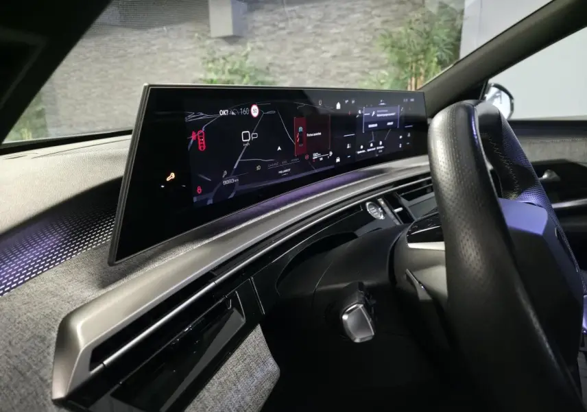 Vue intérieure côté conducteur du tableau de bord numérique panoramique et volant perforé noir du Peugeot 3008 gris 2025.