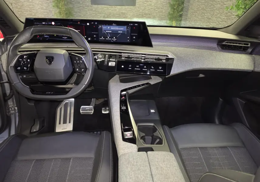 Vue intérieure avant du Peugeot 3008 gris 2025, tableau de bord avec écran panoramique et volant compact cuir noir.