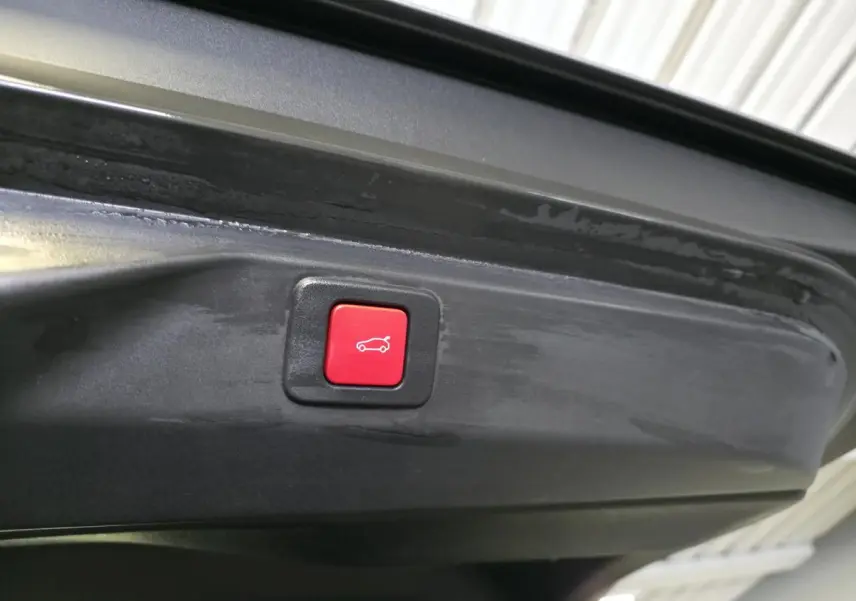 Bouton rouge de fermeture électrique du hayon visible sur l'intérieur du coffre d'un Peugeot 3008 gris.