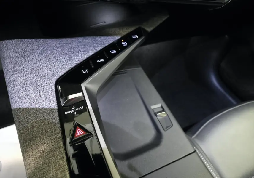 Vue rapprochée de la console centrale tissu gris et noir laqué du Peugeot 3008 Hybrid 2025 avec commandes tactiles et bouton Drive Mode.