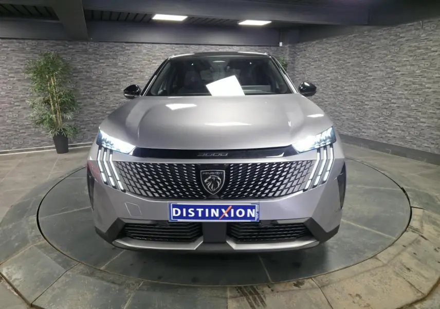 Vue frontale d'un Peugeot 3008 gris métallisé 2025 avec calandre noire à motif géométrique et feux LED griffés allumés.
