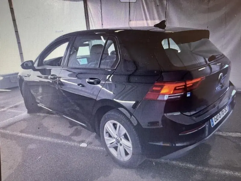 Vue 3/4 arrière droite d'une Volkswagen Golf noire intense nacrée avec feux arrière LED allumés, stationnée en intérieur.