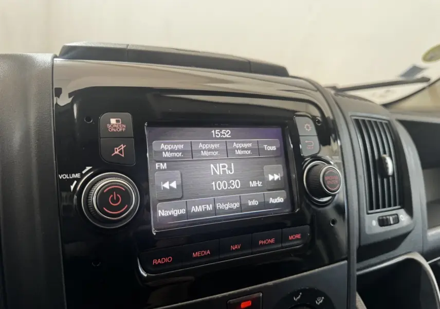Gros plan sur l’écran tactile multimédia noir du tableau de bord du Citroën Jumper blanc, affichant une radio FM NRJ.