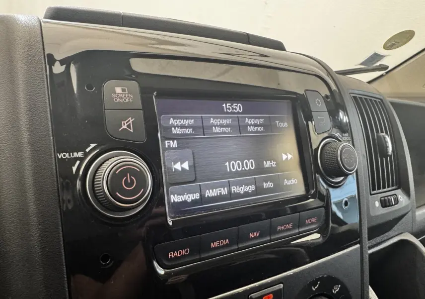 Gros plan sur l’écran tactile multimédia noir du tableau de bord du Citroën Jumper blanc, affichant la radio FM à 100 MHz.