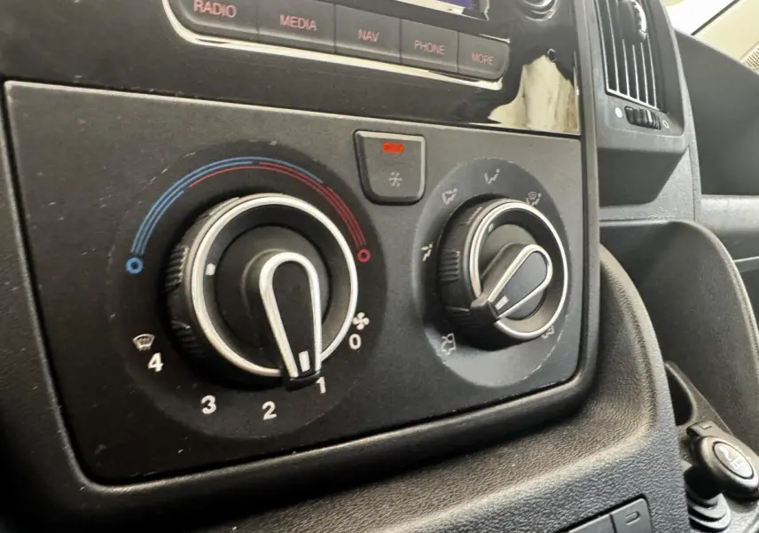 Gros plan sur les commandes de climatisation et la console centrale du Citroën Jumper blanc, intérieur avant.