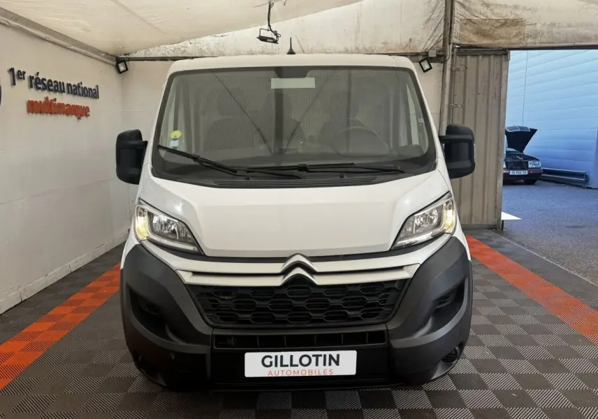 Vue frontale d’un Citroën Jumper blanc 2023 avec calandre noire et phares allumés dans un garage.