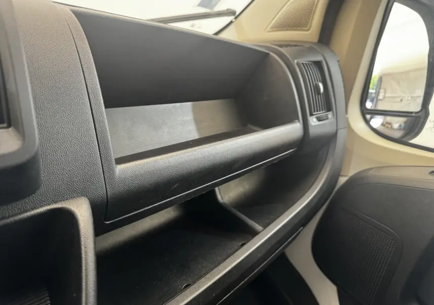 Vue intérieure côté passager du tableau de bord noir avec rangements ouverts et partie de la portière beige du Citroën Jumper 2023.