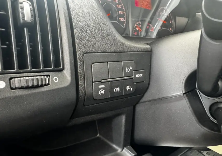 Gros plan sur les commandes d’éclairage et tableau de bord noir du Citroën Jumper 33 L1H1 blanc, vue intérieure côté conducteur.