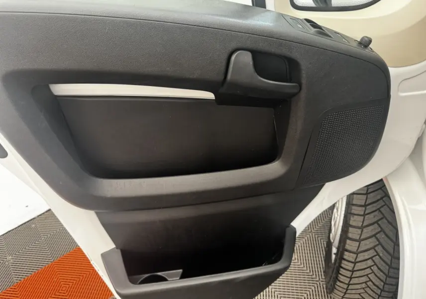 Vue rapprochée de la porte avant gauche blanche du Citroën Jumper 2023 avec poignée noire et rangement intégré.
