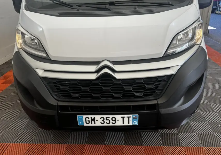 Vue frontale rapprochée du Citroën Jumper blanc avec calandre noire et phares allumés sur sol à damier noir et orange.