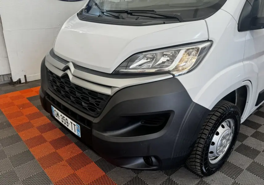 Vue 3/4 avant droit d’un Citroën Jumper blanc avec pare-chocs noir et jante acier sur sol damier orange et gris.