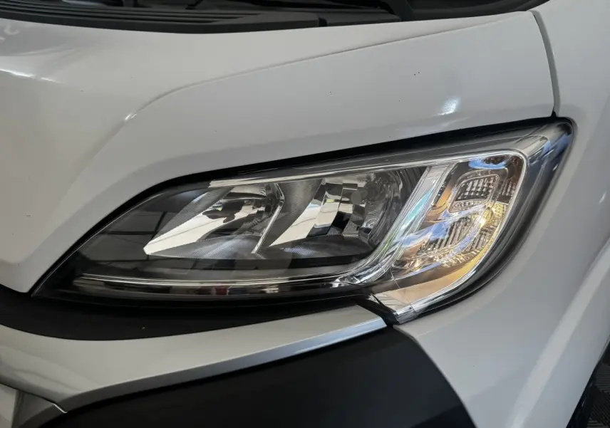 Gros plan sur le phare avant droit du Citroën Jumper blanc 2023, mettant en valeur son design moderne et ses détails chromés.