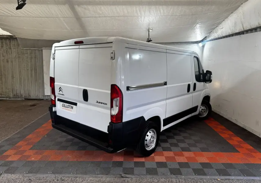 Vue 3/4 arrière droite d’un utilitaire Citroën Jumper blanc stationné en intérieur sur sol à damiers gris et orange.