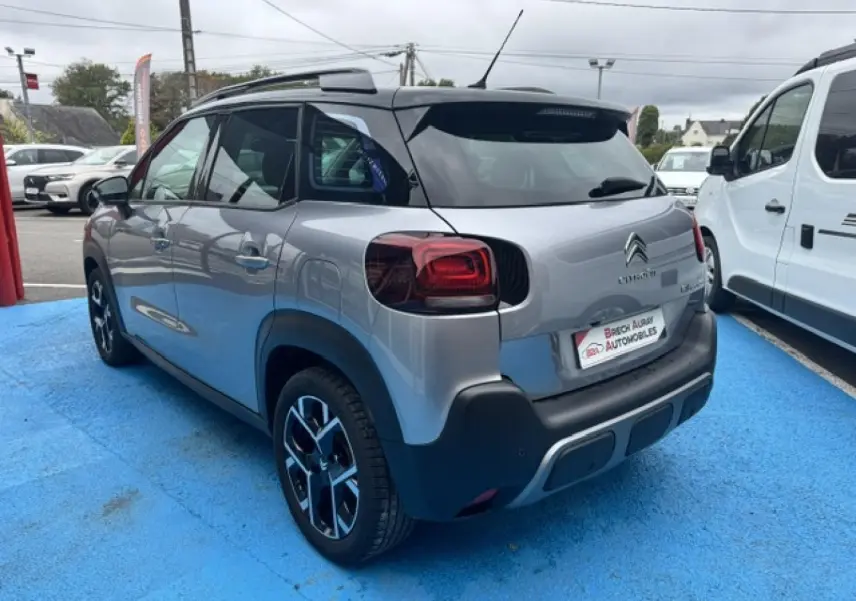Vue 3/4 arrière droite d'un Citroën C3 Aircross gris acier avec barres de toit et jantes alu noires.