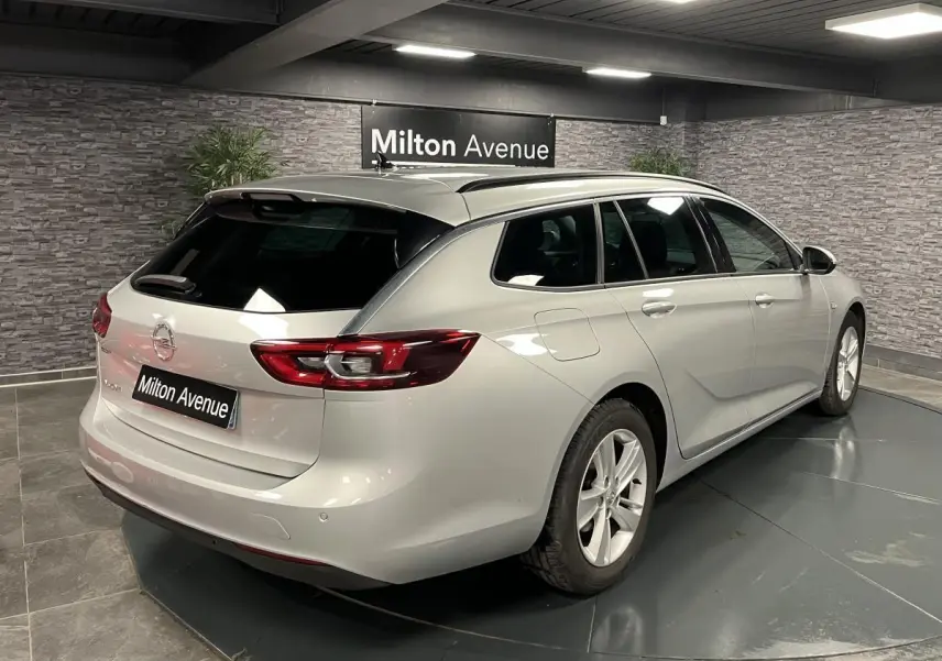 Vue 3/4 arrière droite d'une Opel Insignia Sports Tourer gris métallisé avec vitres arrière surteintées en intérieur showroom.