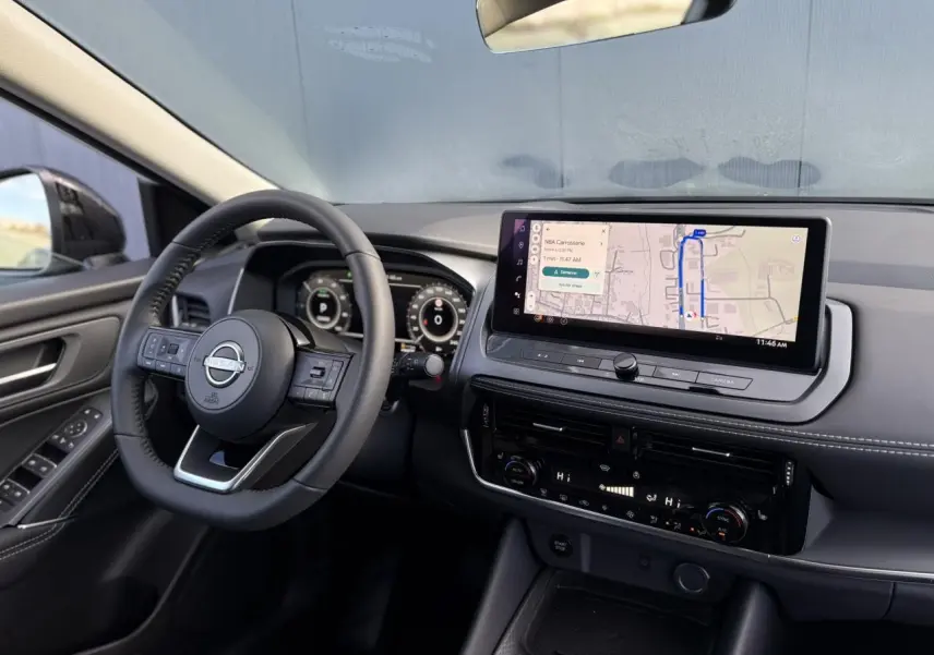 Vue intérieure côté conducteur du Nissan Qashqai blanc nacré 2025, tableau de bord avec écran tactile et volant cuir.