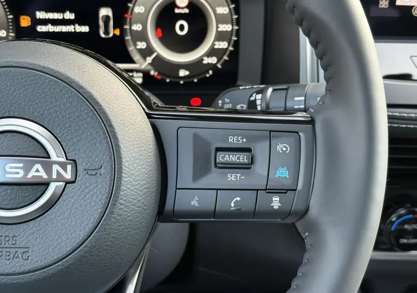 Gros plan sur le volant cuir du Nissan Qashqai blanc nacré, avec commandes de régulateur et affichage numérique en arrière-plan.