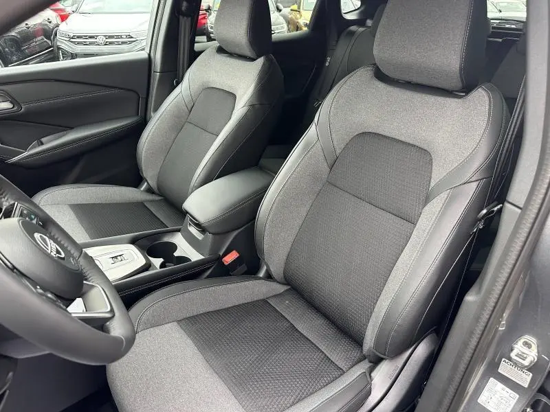 Vue intérieure côté conducteur du Nissan Qashqai Hybrid e-POWER 2025, sièges tissu gris avec console centrale et volant visibles.