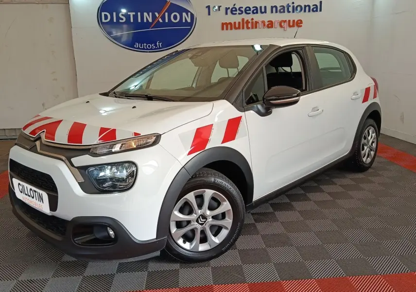 Vue 3/4 avant gauche d'une Citroën C3 blanche avec bandes rouges distinctives sur capot et ailes, en intérieur showroom.