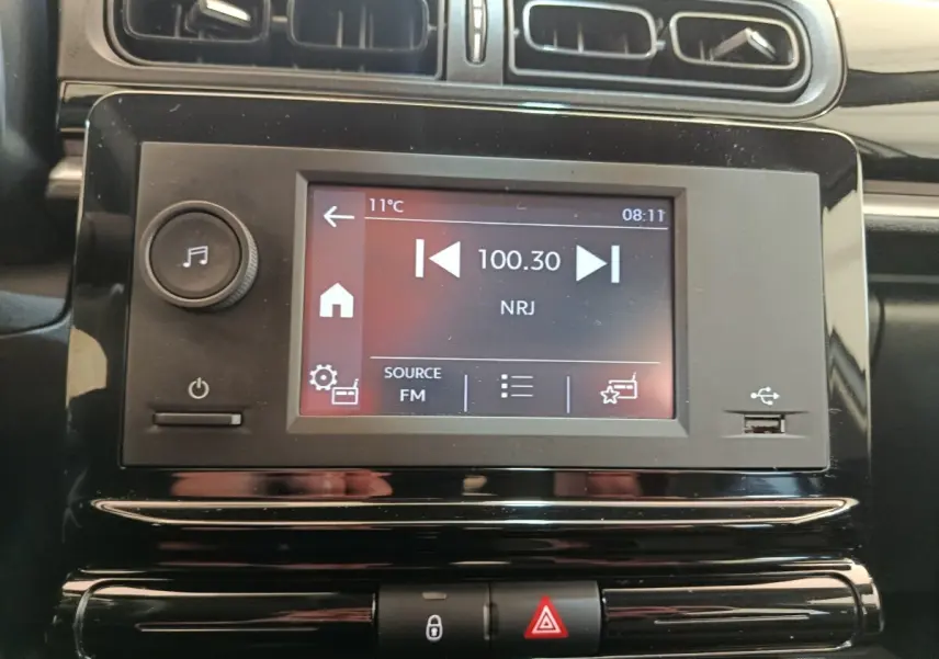 Vue rapprochée de l’écran tactile multimédia noir de la Citroën C3 blanc, affichant la radio FM NRJ à 100.30 MHz.