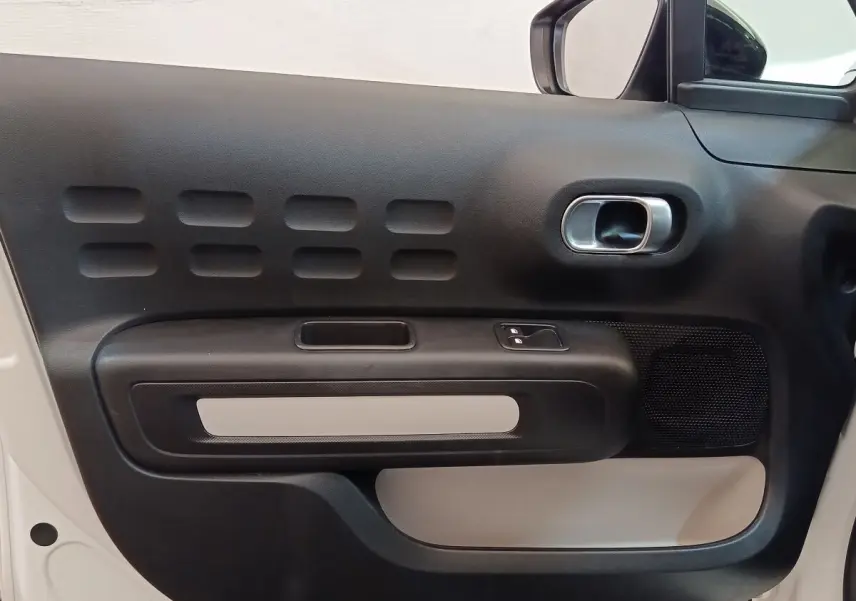 Gros plan sur la porte avant gauche noire et beige de la Citroën C3 blanche, mettant en valeur la poignée et les commandes.
