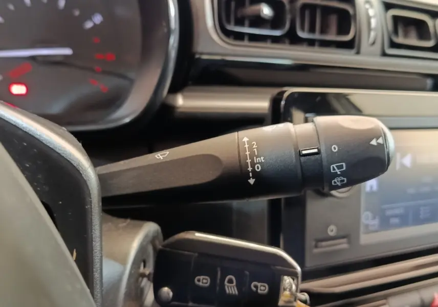 Gros plan sur la commande d’essuie-glace à gauche du volant dans l’habitacle noir de la Citroën C3 blanche.