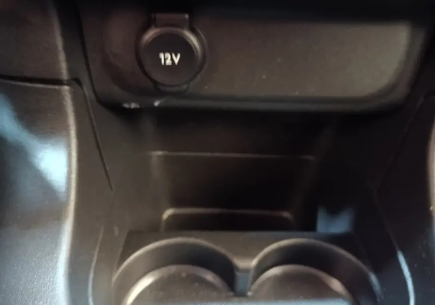 Gros plan sur la prise 12V et porte-gobelets noirs dans l'habitacle d'une Citroën C3 blanche.