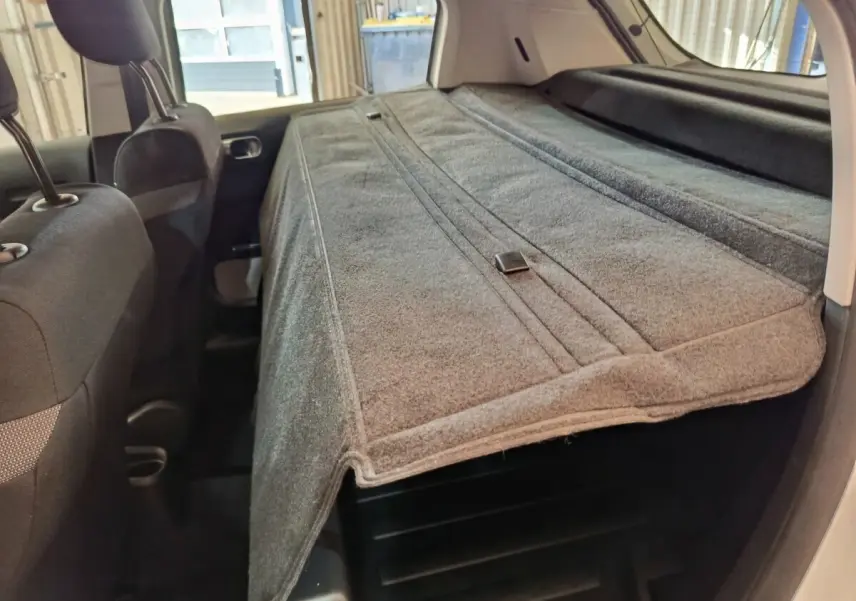 Vue intérieure arrière de la Citroën C3 blanche, mettant en valeur la banquette rabattue et la tablette de coffre grise.