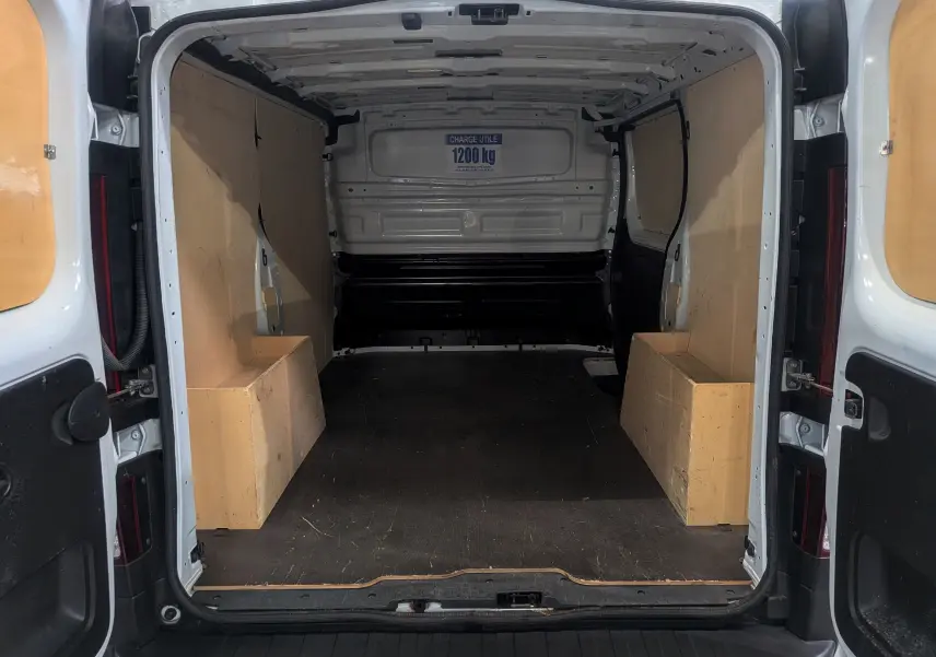 Vue arrière intérieure du Renault Trafic Fourgon blanc minéral 2024, montrant l'espace de chargement avec panneaux bois et capacité 1200 kg.
