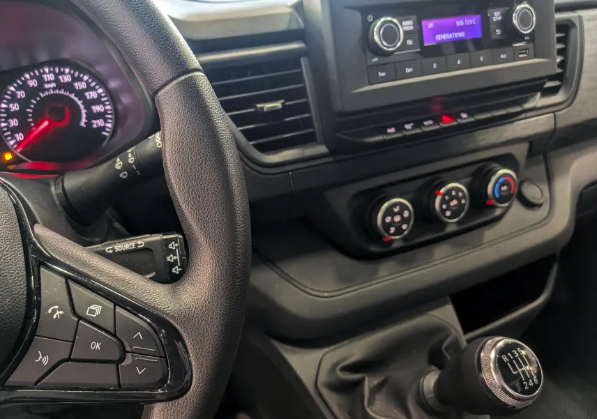 Vue intérieure centrée sur le volant et la console centrale du Renault Trafic Fourgon blanc, avec levier de vitesses manuel visible.