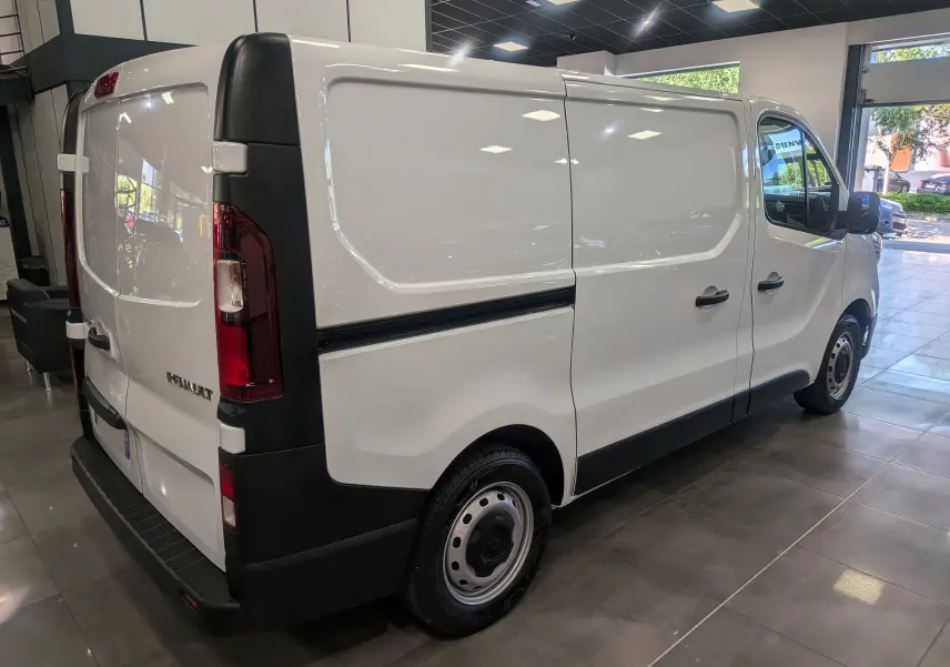 Renault Trafic Fourgon blanc minéral vu en 3/4 arrière droit, avec portes latérales et arrière fermées en intérieur showroom.