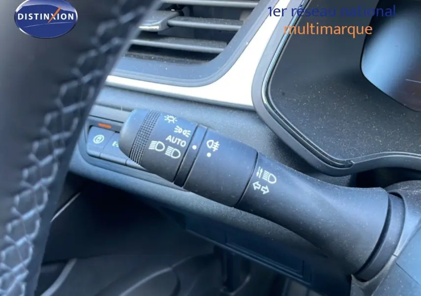 Gros plan sur la commande des phares et clignotants à gauche du volant dans l'habitacle noir du Renault Captur hybride.