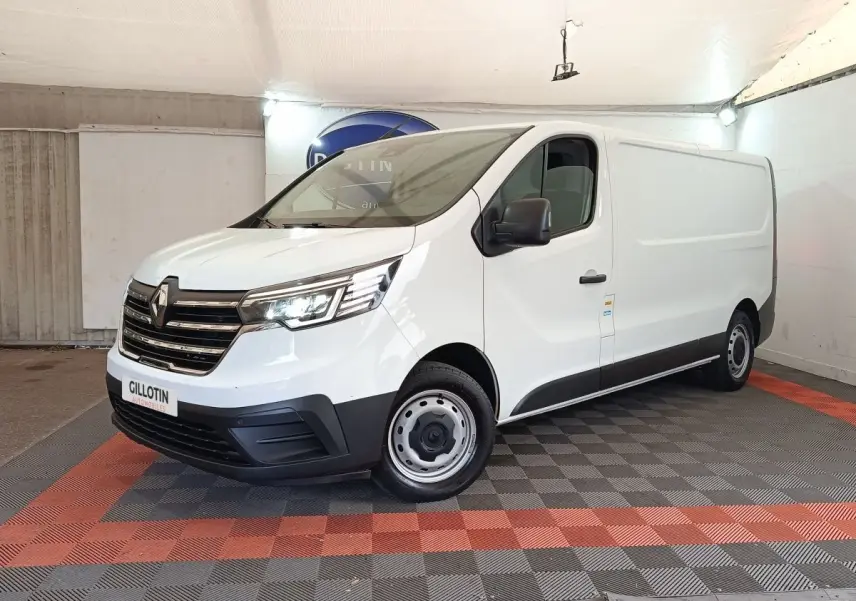 Renault Trafic Fourgon blanc vu en 3/4 avant droit, avec calandre chromée et phares LED allumés dans un showroom.