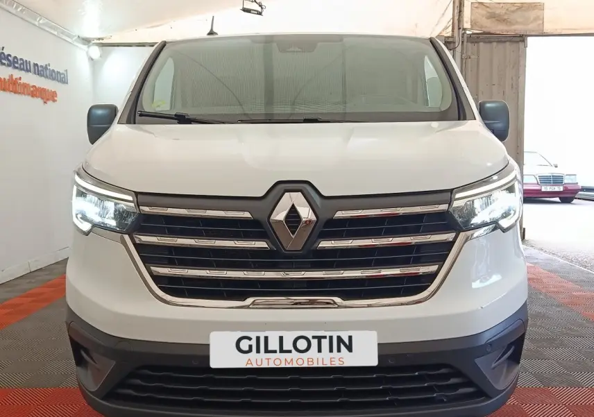 Vue frontale d’un Renault Trafic Fourgon blanc 2023 avec calandre chromée et feux LED allumés.