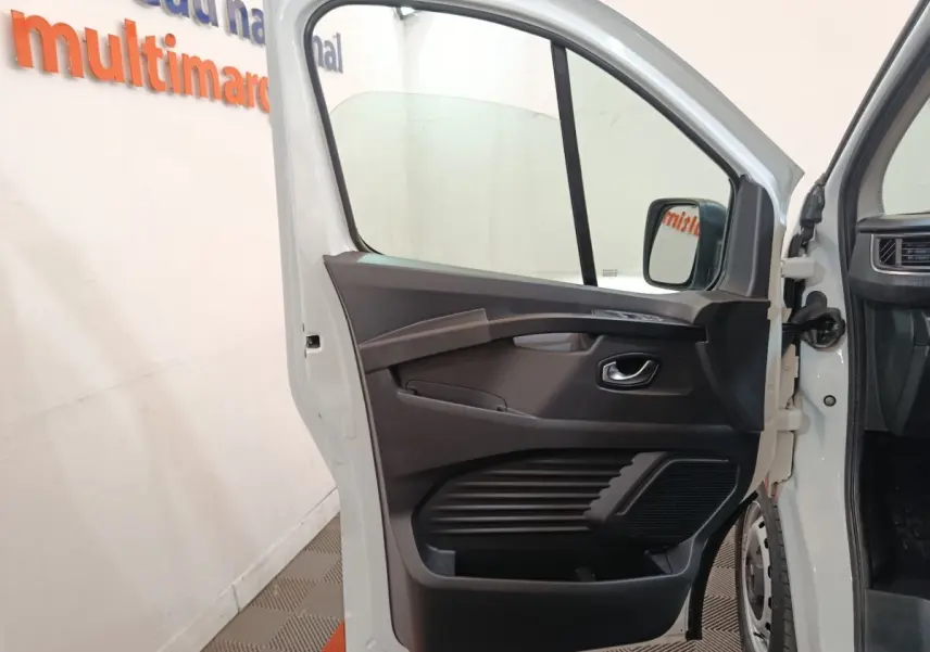 Vue rapprochée de la porte avant gauche ouverte d’un Renault Trafic blanc, montrant la garniture intérieure noire.
