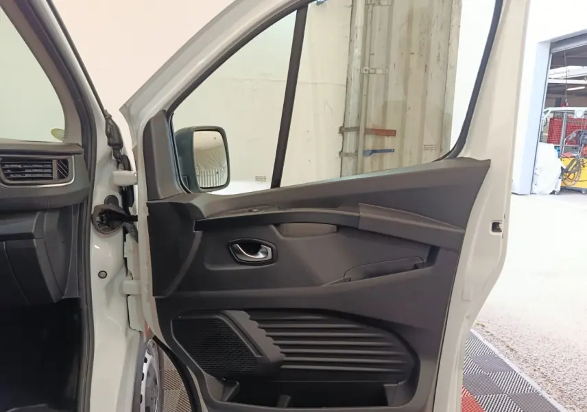 Vue intérieure de la porte avant gauche ouverte d’un Renault Trafic Fourgon blanc, avec panneau noir et poignée intégrée.
