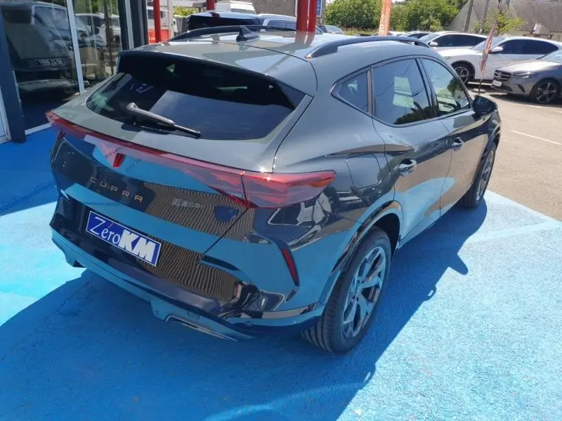 Vue 3/4 arrière droite d'un CUPRA Formentor bleu Fjord avec feux arrière LED et jantes alu foncées sur sol bleu.