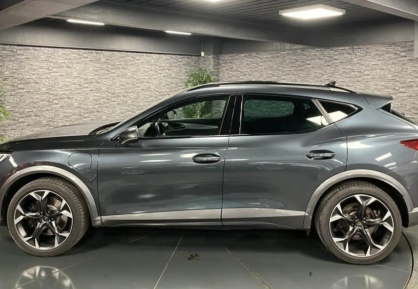Profil côté gauche d'un CUPRA Formentor gris magnétique 2023 avec jantes alliage 19 pouces et prises de recharge visibles.