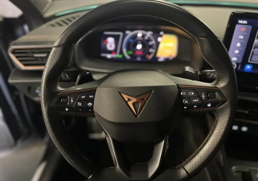 Gros plan sur le volant sport en cuir noir avec logo cuivre du CUPRA Formentor 1.4 e-Hybrid 2023, tableau de bord digital en arrière-plan.