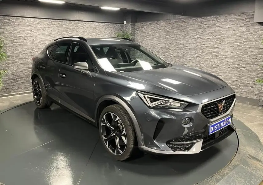 Vue 3/4 avant droit d'une CUPRA Formentor gris magnétique avec jantes noires et détails chromés, en intérieur showroom.