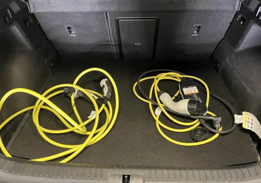 Coffre ouvert d'une CUPRA Formentor gris avec câbles de recharge jaune pour hybride rechargeable visibles.